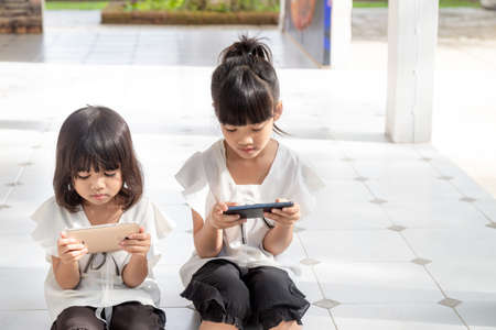 Sibling girls watching their smartphones on white background. Social concept about new technology people addictionの写真素材