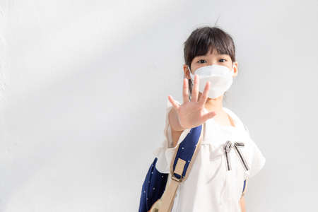 Back to school.Little Asian girl wearing a mask for protection. show stop hands gesture to stop coronavirus outbreak.の写真素材