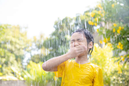 Happy Asian little child girl having fun to play with the rain in the sunlightの写真素材