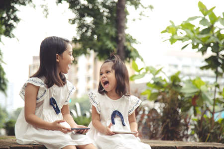 Concept kids and gadgets. Two little girls siblings sisters look at the phone and smile. They hold a smartphone watch videos, learn, play games, speak online. Internet for children. Parental controlの写真素材