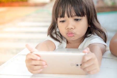 Little Asian girl using smart phone at cafe. Natural light outdoor lifestyle.の写真素材