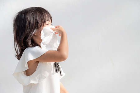 Asian child girl sick with sneezing on the nose and cold cough on tissue paper because weak or virus and bacteria from dust weather and kindergarten and preschoolの写真素材