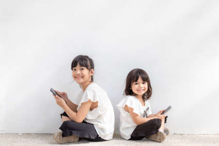 Sibling girls enjoy using smartphones on white background, the Concept of communication technology and peopleの写真素材