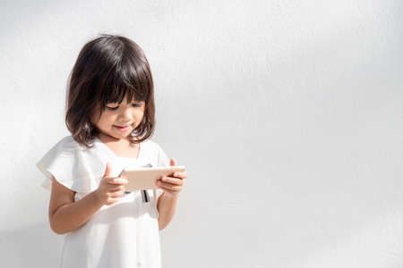 A little girl is concentrated on the phone, look at the smartphone, technology concept for children, profile view, isolated on white background, copy spaceの写真素材
