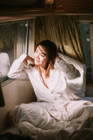 Beautiful young woman in a white shirt in the bedroom at homeの写真素材