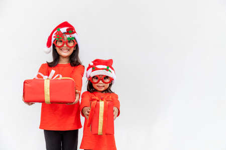 Sibling Asian girls in red Santa hat with gift boxes on white background.の写真素材