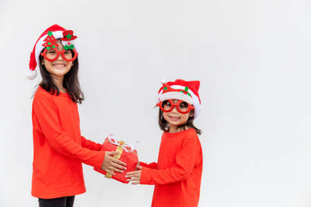 Sibling Asian girls in red Santa hat with gift boxes on white background.の写真素材