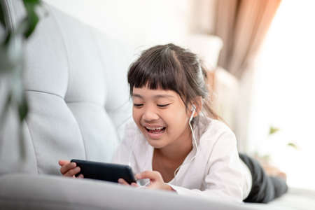 Pretty Asian girl using headphones for listen to music by smartphone in living roomの写真素材