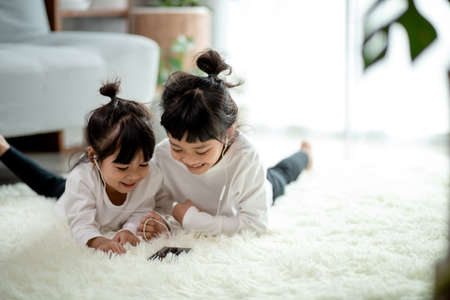 Asian Siblings together on the floor using smartphoneの写真素材