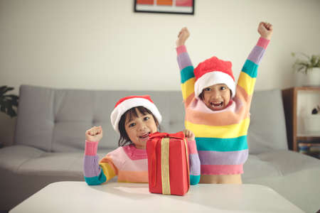 Merry Christmas happy sibling girls with a gift at homeの写真素材