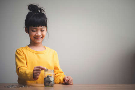 Cute Asian little child girl making stacks of coins . Kid saves money for future education. Money, finances, and people conceptの写真素材