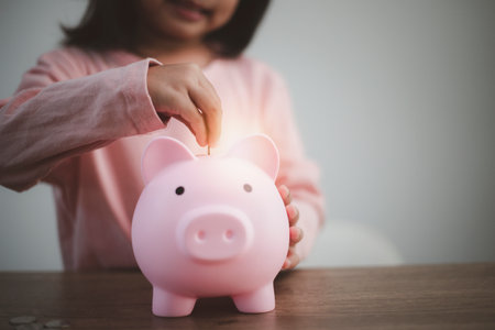Cute asian child girl putting money into piggy bank to save money for the futureの写真素材