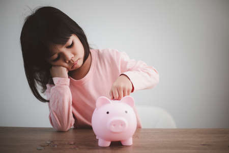 Cute asian child girl putting money into piggy bank to save money for the futureの写真素材