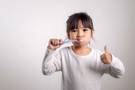 Little cute baby girl cleaning her teeth with toothbrush on white backgroundの写真素材