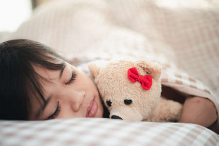 child little girl sleeps in the bed with a toy teddy bear