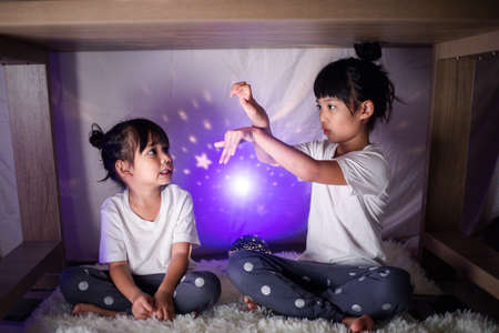 sibling play under a blanket-covered table at nightの写真素材