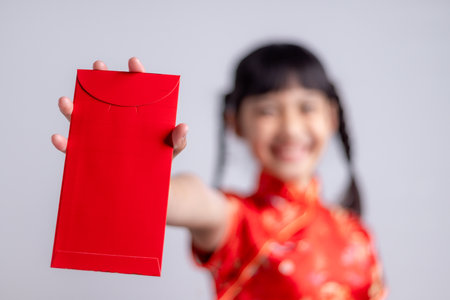 Happy Little Asian girl in Chinese traditional dress smiling and holding a red envelope. Happy Chinese new year concept.の写真素材