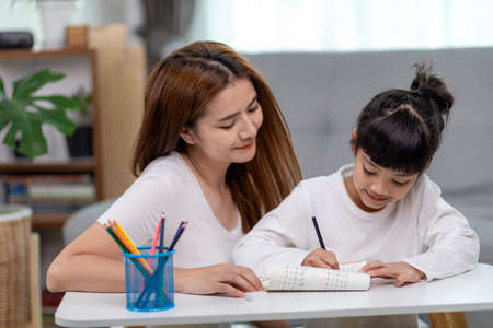 Beautiful Asian woman helping her daughter with homework at home.の写真素材