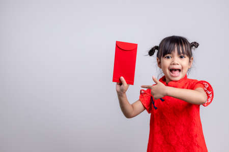 Happy Little Asian girl in Chinese traditional dress smiling and holding a red envelope. Happy Chinese new year concept.の写真素材