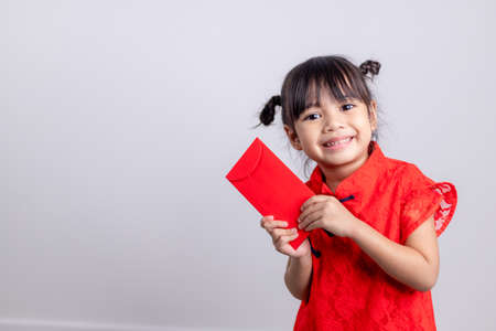 Happy Little Asian girl in Chinese traditional dress smiling and holding a red envelope. Happy Chinese new year concept.の写真素材