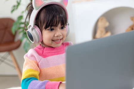 Smiling little Asian girl have a video call distant class with teacher using laptop, social distance...