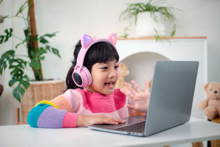 Smiling little Asian girl have a video call distant class with teacher using laptop, social distance...