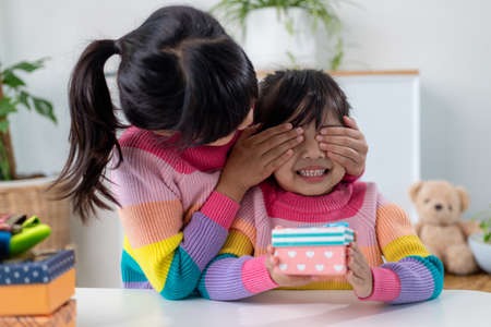 Little girl making present to little happy kid girl holding gift box,  closing eyes of cute smiling ...
