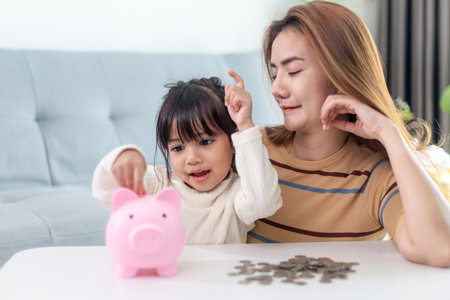 Mother and daughter putting coins into piggy bank. Family budget and savings concept. Junior Savings Account conceptの写真素材