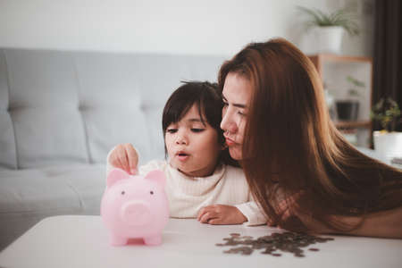Mother and daughter putting coins into piggy bank. Family budget and savings concept. Junior Savings Account conceptの写真素材