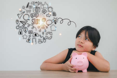 Cute asian child girl putting money into piggy bank to save money for the futureの写真素材
