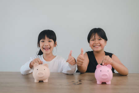 Two asian little girls having fun to put coin into Piggy Bank together,kid saving money for the future conceptの写真素材