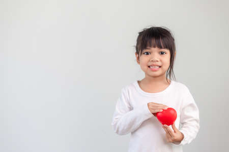 The little girl in a white shirt holding a red heart on a white background. Greeting cards for valentine's day, mother's day, father's day.の写真素材
