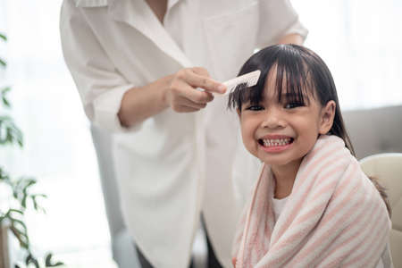Asian Mother cutting hair to her daughter in living room at home while stay at home safe from...