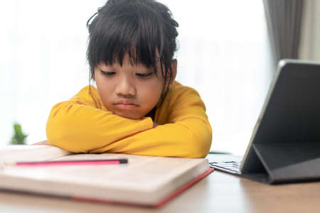 Little Asian girl sitting alone and looking out with a bored face, Preschool child laying head down on the table with sad  bored with homework, spoiled childの写真素材