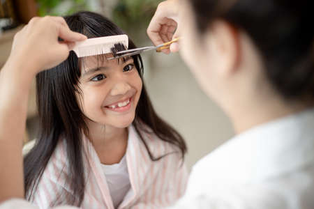Asian Mother cutting hair to her daughter in living room at home while stay at home safe from Covid-19 Coronavirus during lockdown. Self-quarantine and social distancing concept.の写真素材