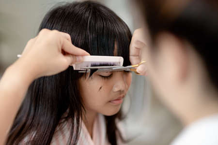 Asian Mother cutting hair to her daughter in living room at home while stay at home safe from Covid-19 Coronavirus during lockdown. Self-quarantine and social distancing concept.の写真素材