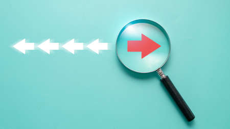 Red arrow inside of magnifier glass and different direction from white arrow for focus business disruption and technology transformation concept.の写真素材