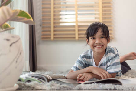 Child reading book at home. Girl lying and reading indoors