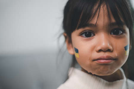 A child with the flag of Ukraine is crying. Sadness longing hope. Children's tears from the war. Evacuation of civilians. Freedom to Ukraineの写真素材