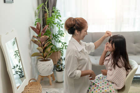 Asian Mother cutting hair to her daughter in living room at home while stay at home safe from Covid-19 Coronavirus during lockdown. Self-quarantine and social distancing concept.の写真素材