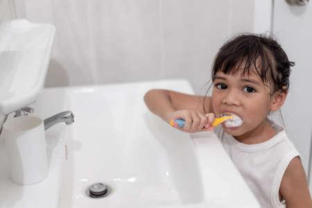 Little cute baby girl cleaning her teeth with a toothbrush in the bathroomの写真素材