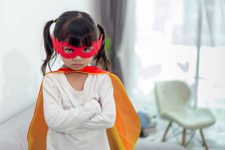 child girl in a super hero costume with mask and red cloak at homeの写真素材