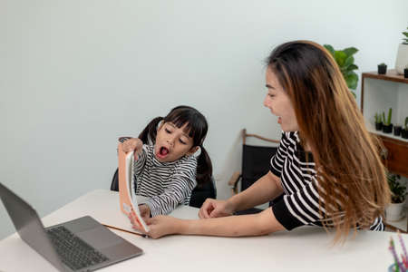 Asian little young girl kid learning online class at home with mother. Preschool child use laptop...