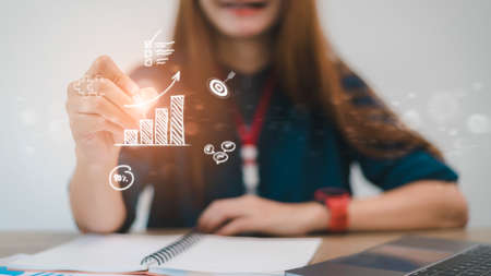 Businesswoman draws an increasing trend arrow and a rising chart from plan to goal. It is a...