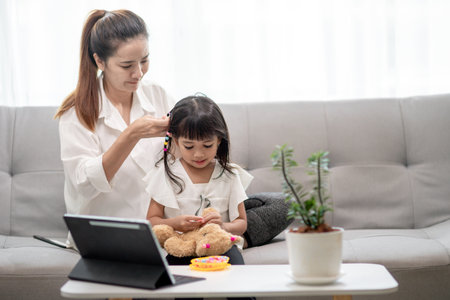 Young Asian mother tying daughter's hairの写真素材