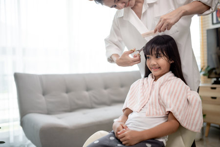 Asian Mother cutting hair to her daughter in living room at home while stay at home safe from...