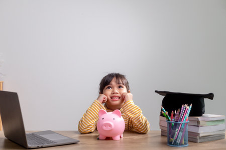 Asian little girl wearing a graduation cap with a pink piggy bank, Saving money, investment the future,の写真素材