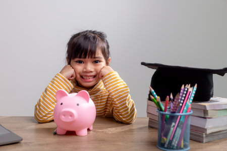 Asian little girl wearing a graduation cap with a pink piggy bank, Saving money, investment the future,の写真素材