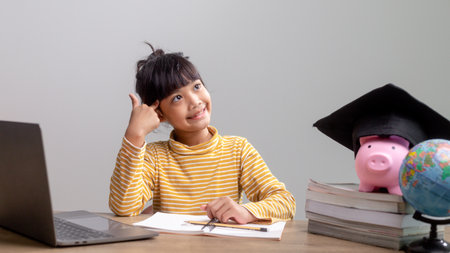 Asian little girl wearing a graduation cap with a pink piggy bank, Saving money, investment the future,の写真素材