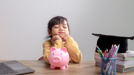 Asian little girl wearing a graduation cap with a pink piggy bank, Saving money, investment the future,の写真素材